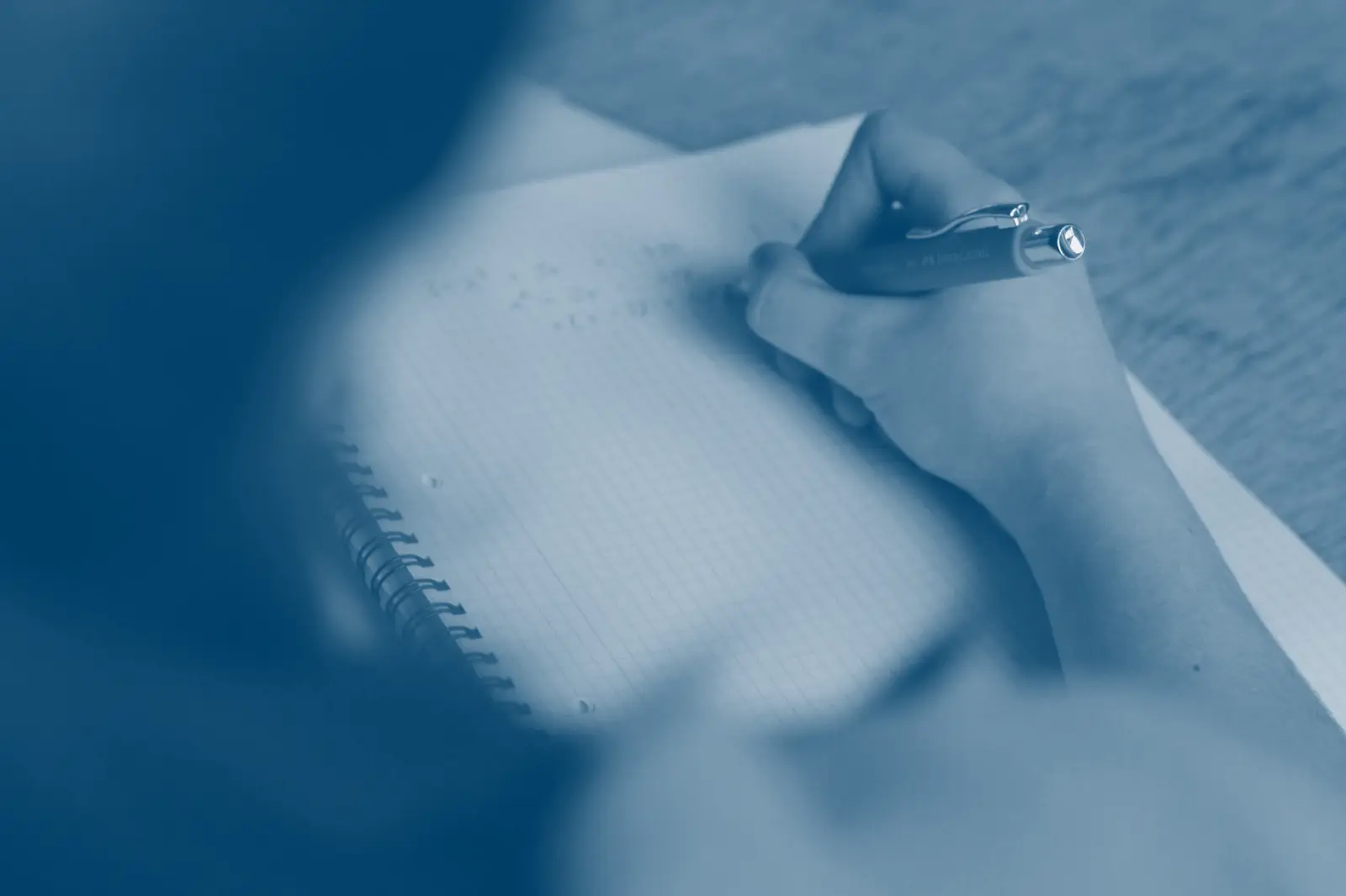 A close-up of hands working through mathematics in a notebook, pen on the page.